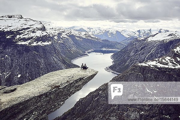 Paar sitzt auf einer Felsplattform auf der Trolltunga und blickt über die Fjordlandschaft  Trollzunge  bei Odda  Provinz Hordaland  Vestland  Norwegen  Europa
