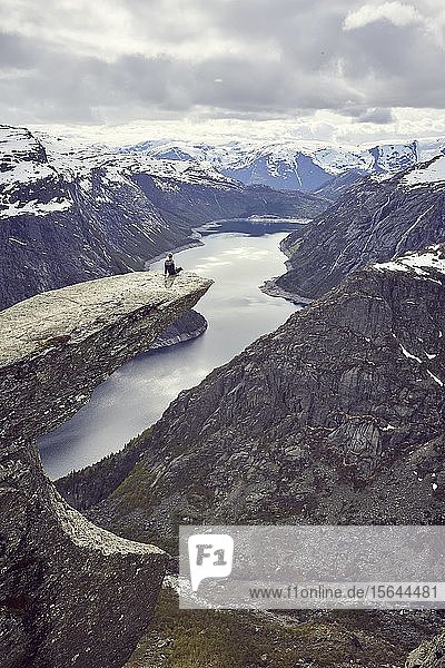 Woman sits on a rock platform on the Trolltunga and looks over fjord landscape  Troll tongue  near Odda  province Hordaland  Vestland  Norway  Europe