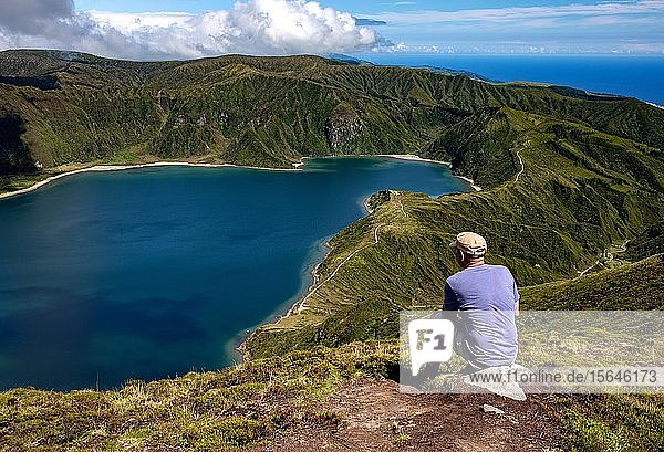Mann sitzt auf einem Stein und schaut auf den See  Lagoa Fogo  Feuerlagune  Insel São Miguel  Azoren  Portugal  Europa