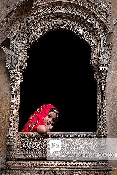 Junges Mädchen schaut aus einem Fenster eines alten Haveli  Jaisalmer  Rajasthan  Indien  Asien