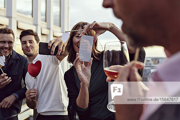 Geschäftskollegen machen Erinnerungen beim Fotografieren mit Smartphones bei Feierlichkeiten nach der Arbeit auf der Terrasse