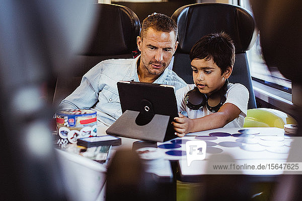 Mid adult man with son looking at digital tablet while sitting in passenger train