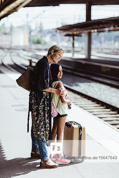 Lächelnde Mutter und Tochter warten auf dem Bahnsteig am Bahnhof