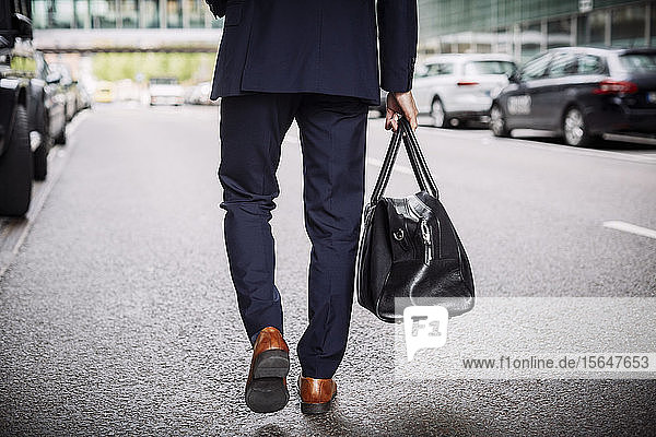 Low section of male lawyer carrying bag while walking on street