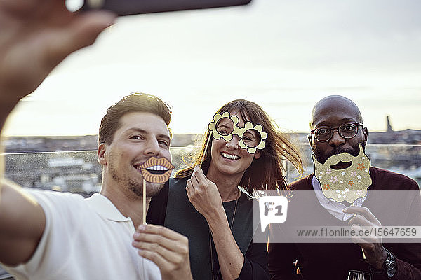 Lächelnde Geschäftskollegen  die sich mit Requisiten vergnügen  während sie bei einer Party auf der Terrasse Selbstgefälligkeit zeigen