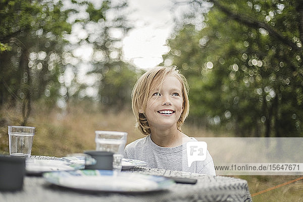 Lächelndes Mädchen schaut weg  während es im Wald am Tisch sitzt