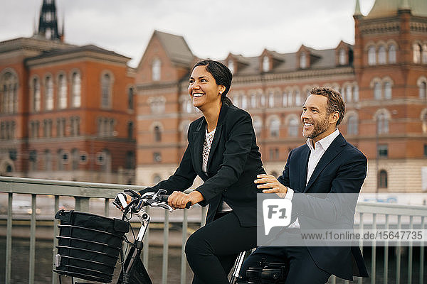 Smiling businesswoman and businessman traveling on bicycle in city