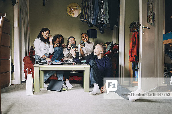 Cheerful friends talking while looking at smart phone in living room