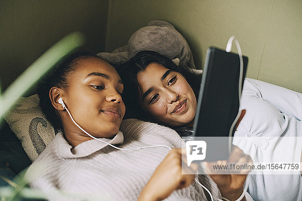 Weibliche Teenager die zu Hause im Bett liegend Musik auf einem digitalen Tablet hören