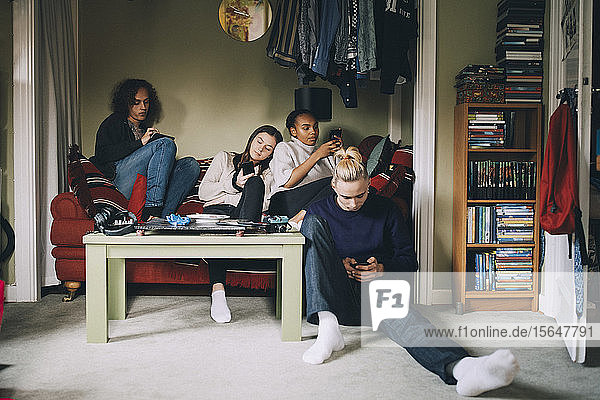 Abgelenkte Freunde benutzen Smartphones  während sie zu Hause zusammen sitzen