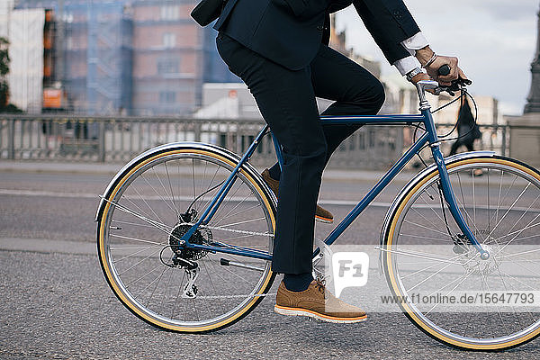Low section of businessman riding bicycle on street in city
