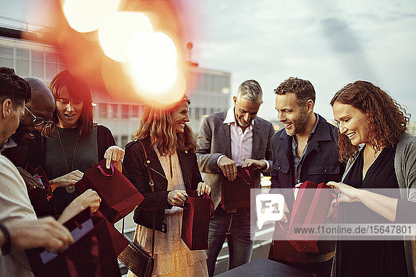 Glückliche Geschäftskollegen kontrollieren Geschenktüten  während sie auf der Terrasse eine Büroparty feiern