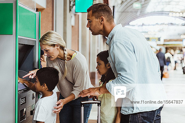 Familie sieht einen Jungen an  der am Bahnsteig des Bahnhofs eine Fahrkarte kauft