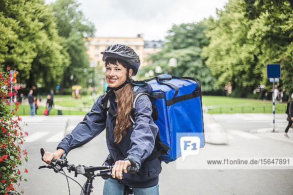 Portrait of smiling food delivery woman with bicycle on street in city