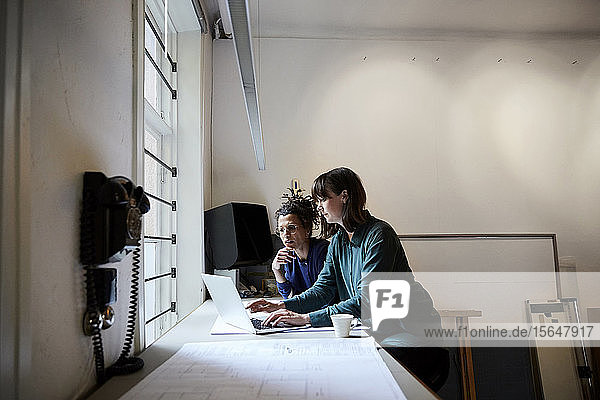Architektinnen diskutieren am Laptop bei Tisch im Büro