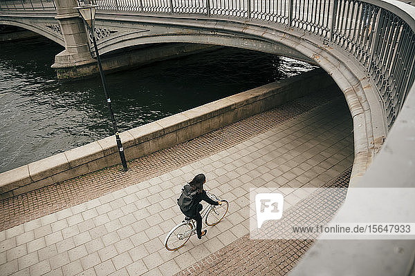 Hochwinkelaufnahme einer Geschäftsfrau  die auf einem Fußweg am Kanal in der Stadt Fahrrad fährt