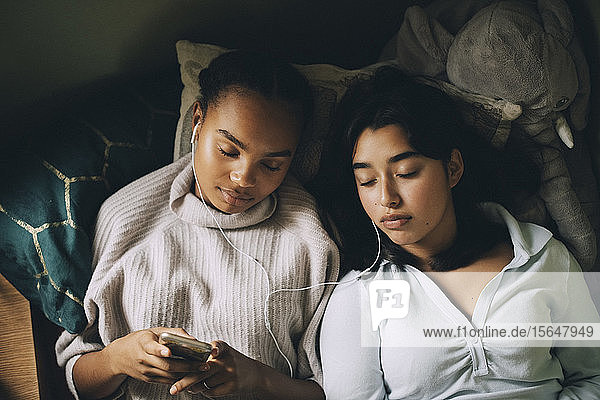 Mädchen im Teenageralter mit geschlossenen Augen die zu Hause im Bett liegend über ein Smartphone Musik hören