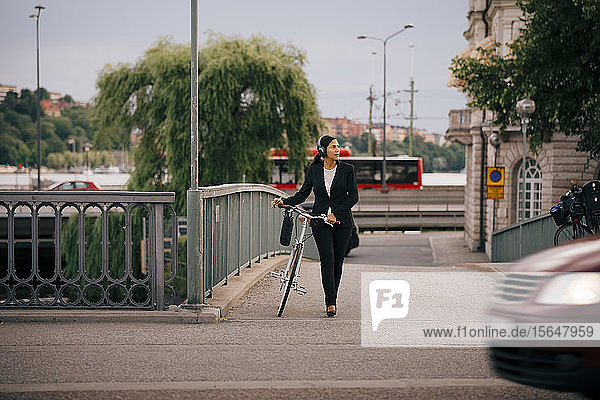 Geschäftsfrau schaut weg  während sie mit dem Fahrrad auf der Brücke in der Stadt läuft