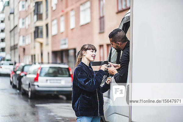 Young woman signing on smart phone being held by male mover in truck