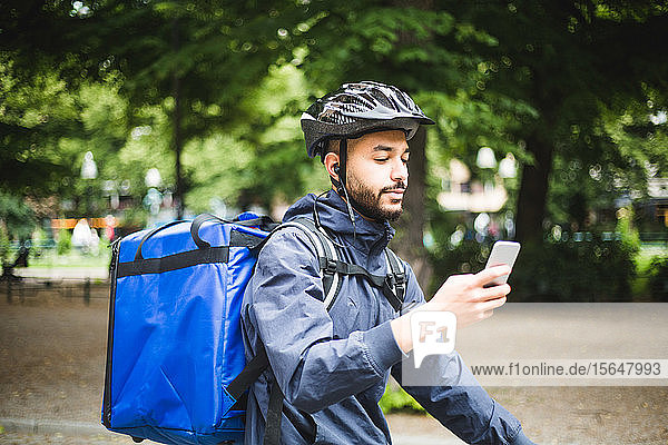 Food delivery man using smart phone on street in city