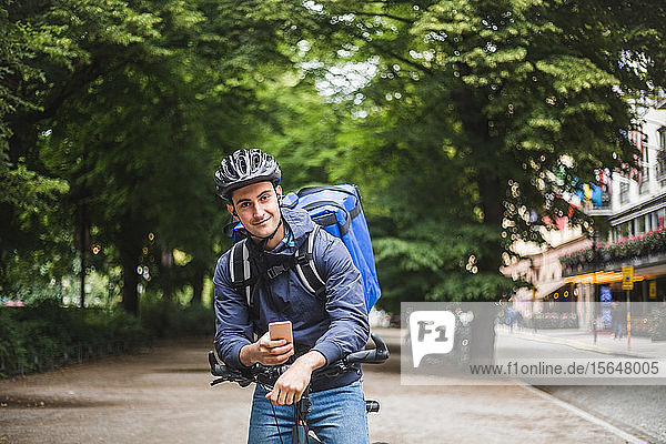 Portrait of confident food delivery man with bicycle in city