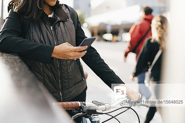 Ein Teil einer Geschäftsfrau  die ein Smartphone benutzt  während sie in der Stadt mit dem Fahrrad steht