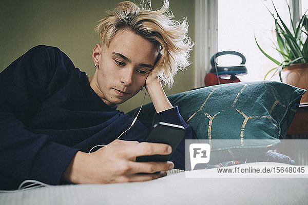 Teenager-Junge hört Musik  während er im Schlafzimmer ein Mobiltelefon benutzt