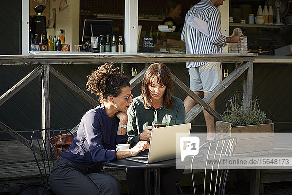 Architektinnen diskutieren über Mobiltelefon im Außencafé