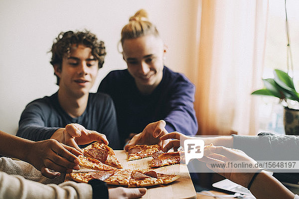Male and female teenage friends taking slices of pizza from tray at home