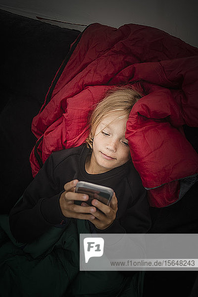 Hochwinkelansicht eines Mädchens  das ein Mobiltelefon benutzt  während es im Zelt liegt
