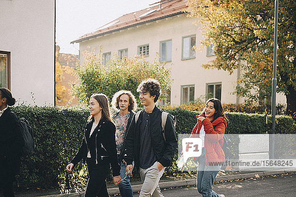 Teenage friends walking together on street in city during sunny day