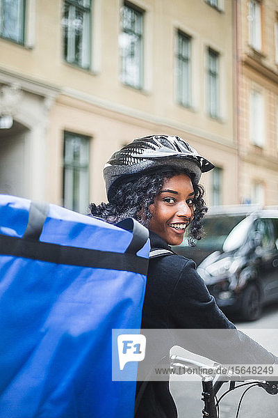Portrait of smiling delivery woman with bag in city