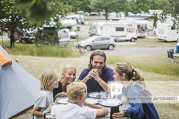 Happy family talking while having food together at table by tent