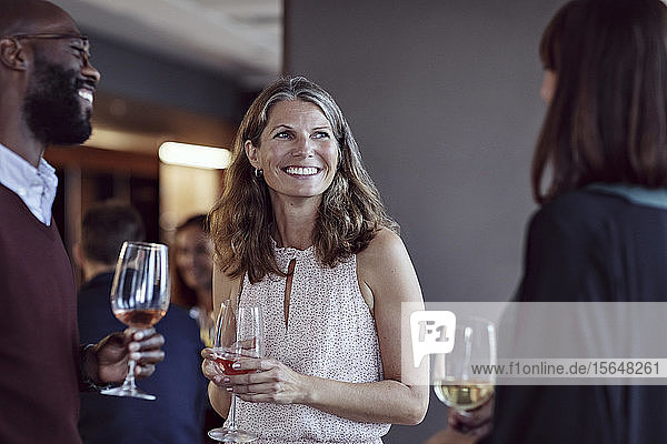 Smiling business people talking over drinks in office party