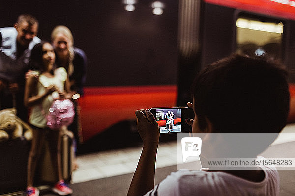 Junge fotografiert Familie auf Smartphone am Bahnsteig