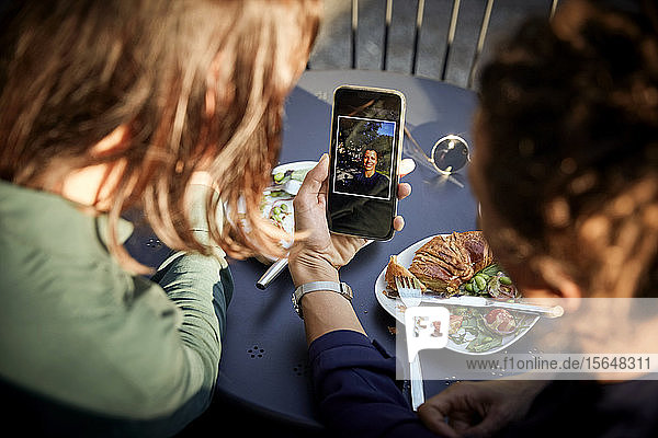 Hochwinkelansicht einer Architektin  die einem Mitarbeiter im Außencafé ein Foto per Mobiltelefon zeigt