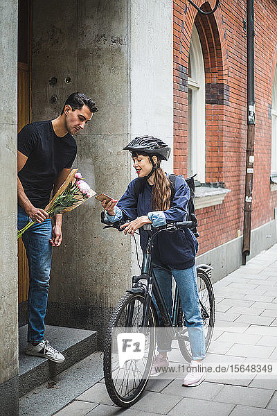 Zustellerin zeigt dem männlichen Kunden während der Blumenübergabe ein Mobiltelefon