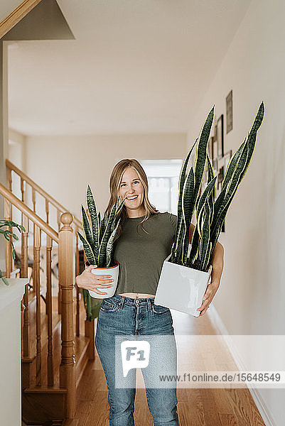 Frau trägt große und kleine Töpfe mit Zimmerpflanzen