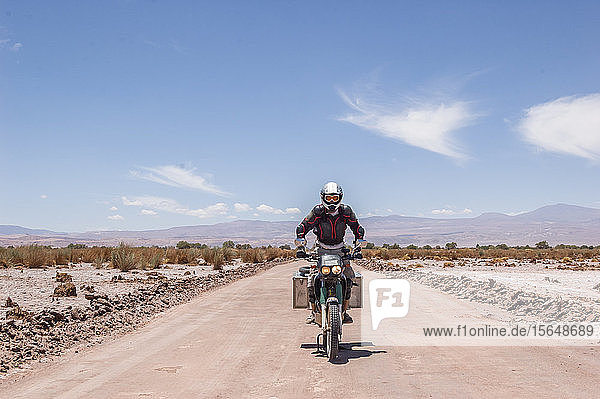 Motorcyclist driving touring motorcycle on dirt road  San Pedro de Atacama  Chile