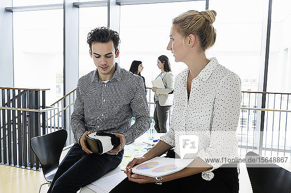 Geschäftsmann mit VR-Headset und Geschäftsfrau im Gespräch im Büro  Kollegen im Hintergrund