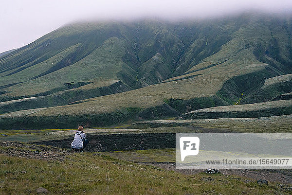 Frau sitzt am Boden und bewundert den Hang  Landmannalaugar  Island