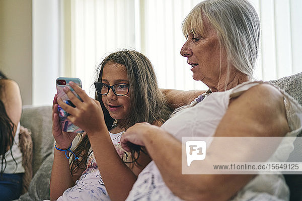 Großmutter schaut ihrer Enkelin beim Spielen von Computerspielen auf dem Sofa zu