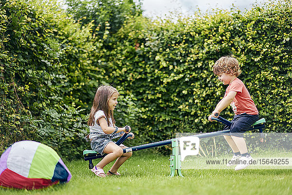 Girl and boy on toy seesaw in garden