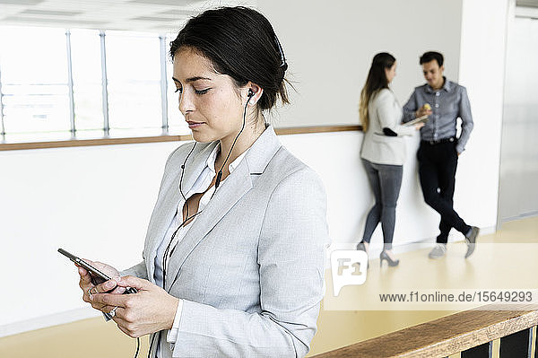 Junge Geschäftsfrau nutzt Smartphone im Büro  Kollegen sprechen im Hintergrund