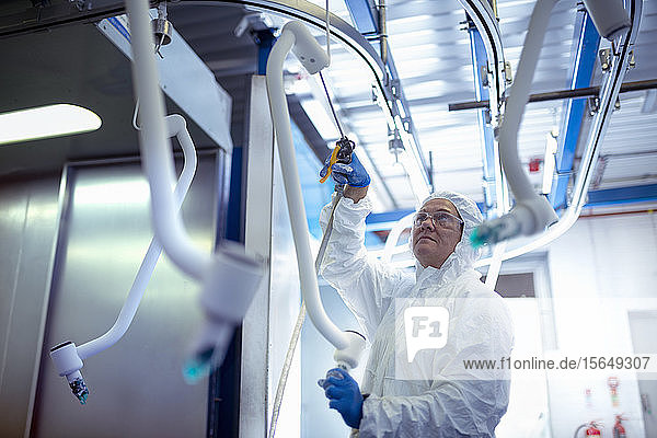 Worker in protective suit cleaning powder coated product in electronics assembly factory