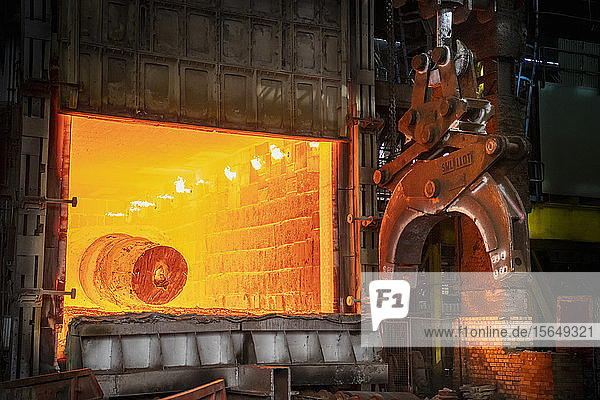 Heat treated red hot steel ingot being lifted by crane in furnace in steelworks