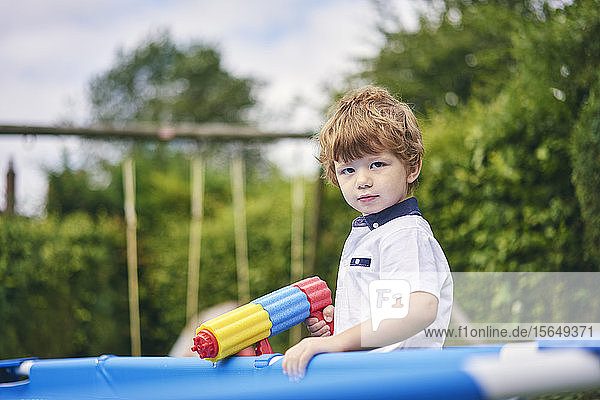 Boy holding water gun by pool