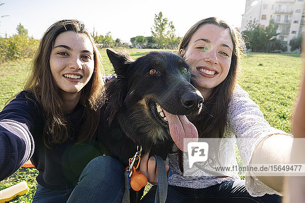 Sisters taking selfie with dog in park