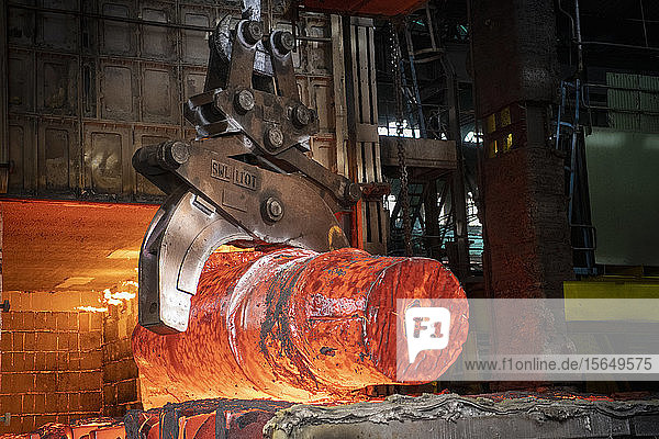 Heat treated red hot steel ingot being lifted by crane in furnace in steelworks