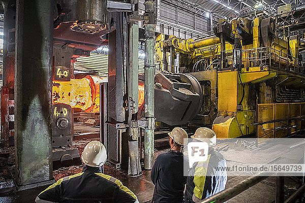 Steelworkers inspecting red hot steel ingot in heavy press in steelworks